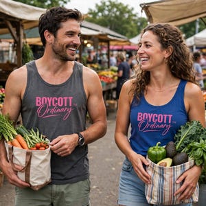 May include: A charcoal grey tank top and a blue tank top, both featuring the pink text "BOYCOTT Ordinary" printed on the front. The charcoal top is worn with olive green shorts, and the blue top is worn with light blue denim shorts.