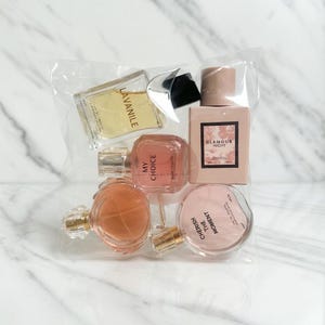 May include: A selection of perfume bottles in a clear plastic bag. The bottles are different shapes and sizes, with colours from clear to pink and peach. Some bottles have labels, including "Lavanile", "My Choice", "Glamour Night", and "Cherish the Moment".