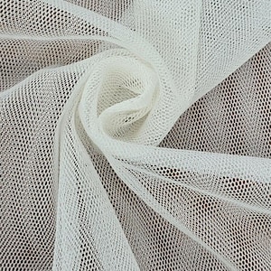 May include: Close-up of white tulle fabric with a net-like pattern. The fabric is draped and swirled, creating a textured effect. The material is a bright white color, and the background is a dark brown.