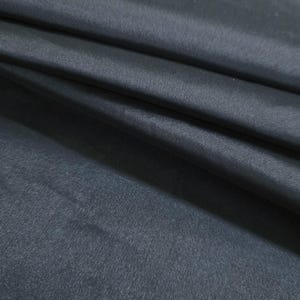 May include: Close-up of a dark gray fabric with a subtle sheen. The material is folded, creating soft shadows and highlights across its surface. The texture appears smooth and possibly silky, suggesting a luxurious textile.