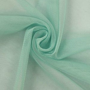 May include: Close-up of a folded piece of mint green tulle fabric. The fabric has a fine, open weave, creating a delicate, see-through texture. The tulle is gathered and folded, showing the fabric's soft, flowing nature. Ideal for crafting, fashion, and decorative projects.