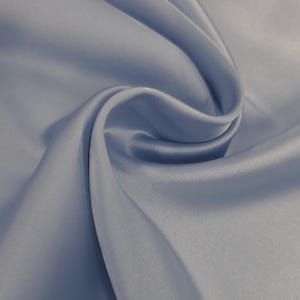 May include: A close-up of a swirl of light blue satin fabric. The fabric has a smooth, shiny texture with soft folds and shadows, creating a sense of depth and movement. The color is a muted, cool tone, suggesting elegance and luxury.