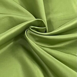 May include: Close-up of a vibrant green fabric with a silky sheen. The material is draped and folded, creating soft shadows and highlights. The color is a bright, fresh green, reminiscent of spring.