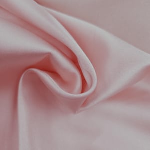 May include: Close-up of a light pink satin fabric with soft folds and a smooth texture. The fabric is draped, creating shadows and highlights that emphasize its sheen. The overall effect is one of elegance and luxury.