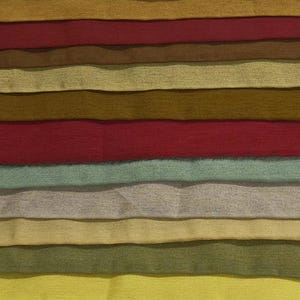 May include: A collection of fabric swatches in various colors, including shades of green, brown, red, and yellow. The swatches are arranged horizontally, showcasing the different textures and hues of the material.