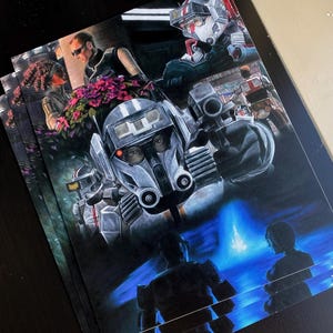 May include: Stacked prints featuring a futuristic sci-fi scene with armored figures and a blue-lit environment. The artwork showcases detailed illustrations of robots and characters in a dark, dramatic style, with a focus on action.