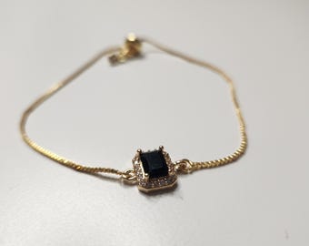 Puede incluir: Pulsera dorada con una piedra negra rectangular en el centro, rodeada de piedras claras más pequeñas. La pulsera de cadena ajustable tiene un diseño delicado, adecuada para el uso diario o ocasiones especiales.