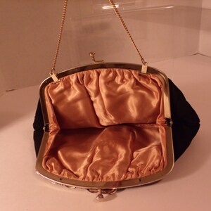 May include: Open black velvet evening bag with a gold-tone metal frame and chain handle. The interior is lined with peach-colored satin fabric. The bag is open, revealing the interior.