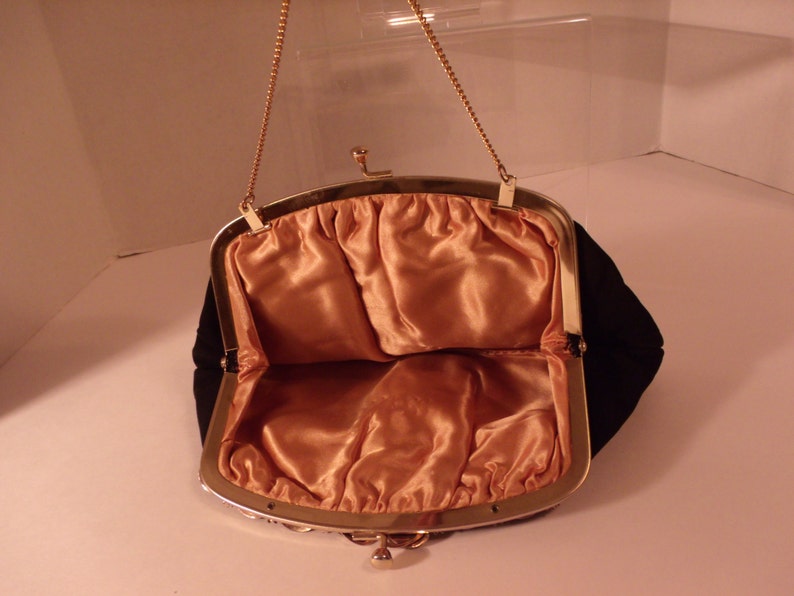 May include: Open black velvet evening bag with a gold-tone metal frame and chain handle. The interior is lined with peach-colored satin fabric. The bag is open, revealing the interior.
