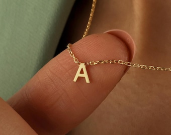 Peut inclure: Un délicat collier en or avec un petit pendentif en forme de lettre "A". Le pendentif est suspendu à une fine chaîne. Le collier est présenté sur un fond doux, soulignant l'élégance simple du bijou.