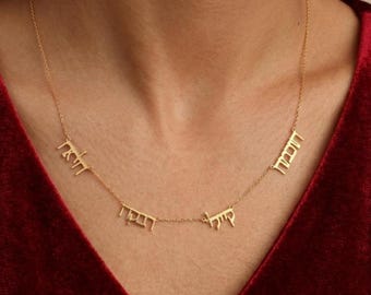May include: A gold-toned necklace featuring a delicate chain with four distinct nameplate pendants written in Hebrew script. The pendants are spaced evenly along the chain, which rests against the neck, creating a layered and personalized appearance.