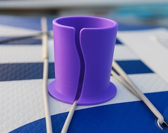 May include: Purple plastic cup holder with a wide base, designed to hold a beverage on a paddleboard or other watercraft.