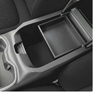 Puede incluir: Una consola de coche negra con un compartimento de almacenamiento abierto y una bandeja extraíble. La consola está hecha de un material oscuro texturizado y está rodeada de asientos de coche negros.