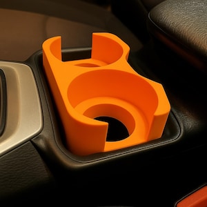 May include: Bright orange car cup holder with two circular openings and a curved design. The cup holder is designed to fit into a car's center console. The cup holder is made of a durable plastic material.