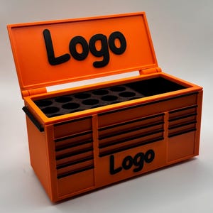 Puede incluir: Una caja de herramientas naranja con detalles negros y la palabra "Logo" en la tapa y el frente. La caja de herramientas está abierta, revelando un interior negro con un inserto de espuma. Tiene un asa a cada lado.
