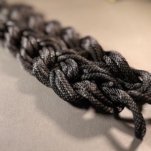 May include: A close-up of a black braided rope, showing the intricate knotting and texture of the material.