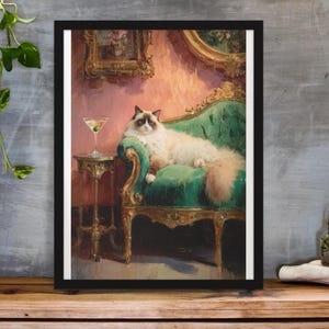 Puede incluir: Impresión artística enmarcada de un gato relajado en una chaise longue de terciopelo verde, con un martini en una mesa auxiliar. El gato tiene un pelaje blanco y marrón esponjoso. El fondo presenta una pared rosa y arte enmarcado en oro.