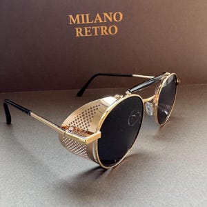 May include: Gold-rimmed sunglasses with black lenses and side shields. The sunglasses have a retro design, with the text "MILANO RETRO" in gold on the background.