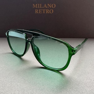 Op de afbeelding: Groene piloten zonnebril met een verlooplens. De zonnebril heeft een donkergroen montuur en pootjes. De tekst "MILANO RETRO" is zichtbaar op de achtergrond.