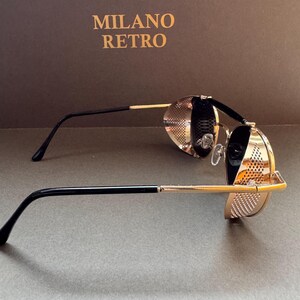 May include: Gold-toned steampunk-style sunglasses with black temples and a perforated design. The sunglasses have round lenses and are set against a brown background with the text "MILANO RETRO".