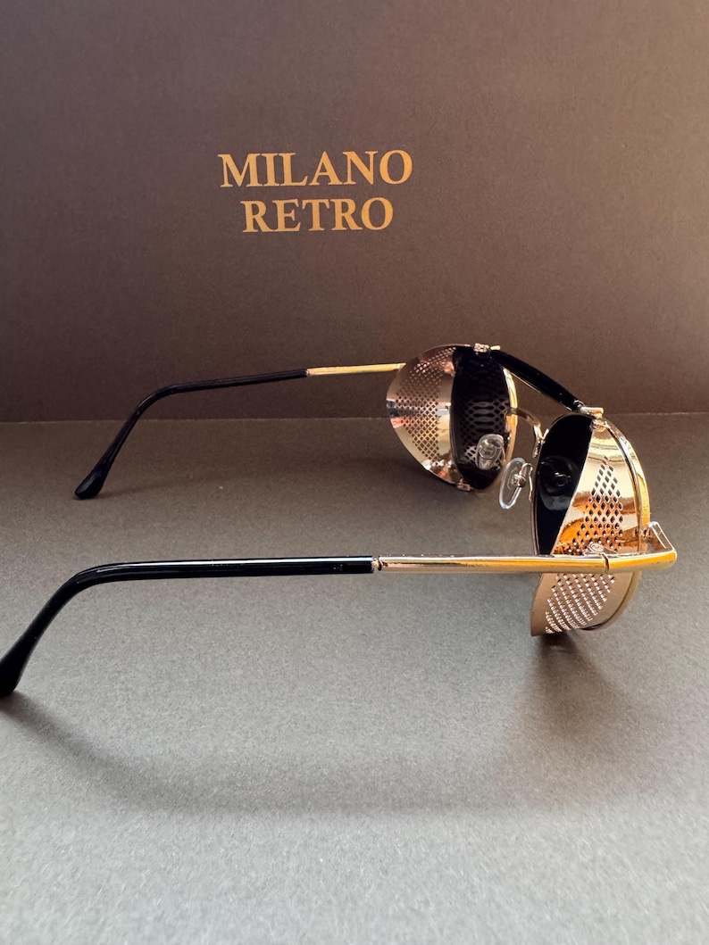 May include: Gold-toned steampunk-style sunglasses with black temples and a perforated design. The sunglasses have round lenses and are set against a brown background with the text "MILANO RETRO".