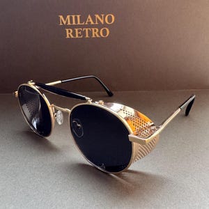 May include: Gold-framed sunglasses with black lenses and side shields. The sunglasses have a retro design with the text "MILANO RETRO" in gold on a brown background.