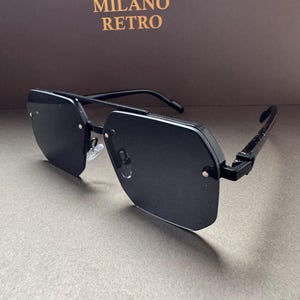 May include: Black sunglasses with a geometric design. The sunglasses have a black frame and lenses. The text "MILANO RETRO" is in gold lettering on the background.