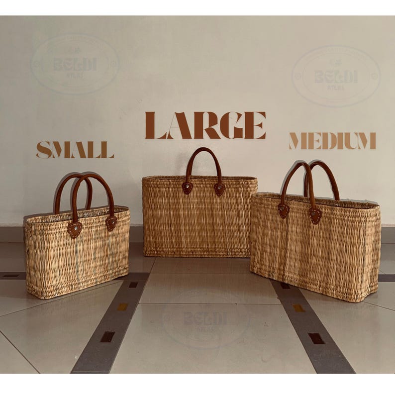 May include: Three woven straw tote bags in varying sizes: small, medium, and large. Each bag features brown leather handles and trim. The bags are displayed against a neutral background with the size labels above them.
