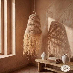 Può includere: Una lampada a sospensione intrecciata con un design svasato a forma di campana e lunghe ciocche sfilacciate. La luce è sospesa a un cavo in una stanza con una tavolozza di colori neutri. L'apparecchio è realizzato con fibre naturali.