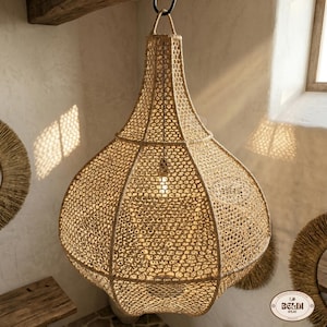 Peut inclure: Un luminaire suspendu beige tissé avec une ampoule à l'intérieur, suspendu à un crochet noir. La lumière a un design texturé distinctif et est suspendue à une poutre en bois. Le luminaire est dans une pièce avec de la lumière naturelle.