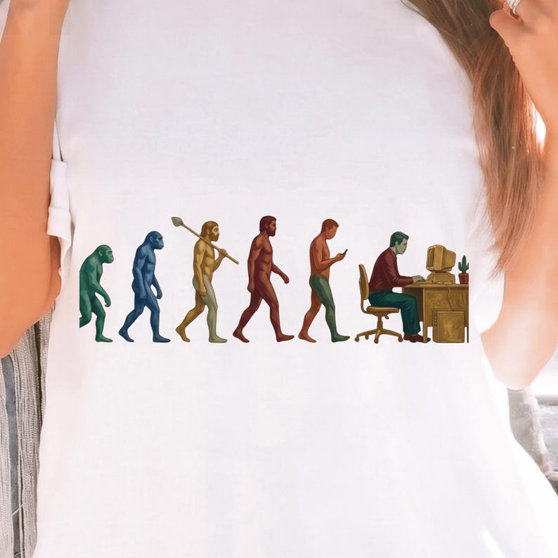 Pode incluir: Uma t-shirt branca com uma impress&atilde;o gr&aacute;fica da evolu&ccedil;&atilde;o humana, come&ccedil;ando com um primata verde e progredindo atrav&eacute;s de v&aacute;rias fases at&eacute; um humano sentado a uma secret&aacute;ria a usar um computador, com um pequeno cato ao lado do monitor.