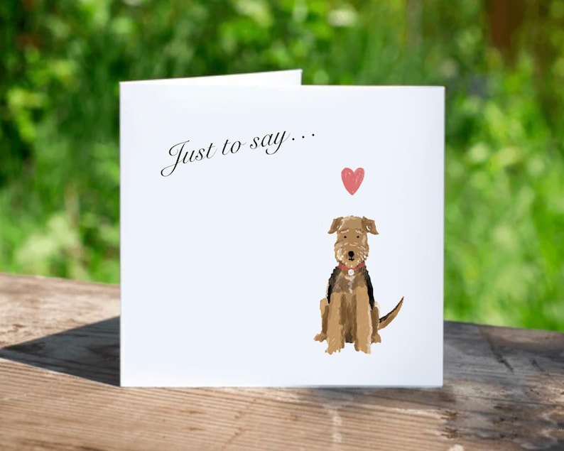 K&ouml;nnte beinhalten: Wei&szlig;e Gru&szlig;karte mit dem Text "Just to say..." und einer Aquarellillustration eines braun-schwarzen Hundes mit einem roten Herz. Die Karte liegt auf einer Holzoberfl&auml;che.