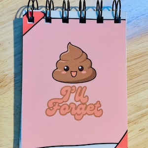 May include: A pink spiral-bound notepad featuring a cartoon poop emoji and the text "I'll Forget" in a retro font. It has black metal binding and a white border.