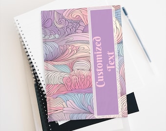 Op de afbeelding: Een stapel notitieboeken, waarvan één met een pastelkleurige bloemenprint en een paars paneel met de tekst "Customized Text". Een pen ligt erbovenop.