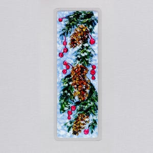 May include: A rectangular bookmark featuring a painted illustration of green pine branches dusted with white snow, three brown pinecones, and clusters of bright red berries against a light blue background with a thin silver border.