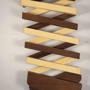 May include: A wooden kitchen utensil holder with a criss-cross design. The holder is made of two different types of wood, one light and one dark.