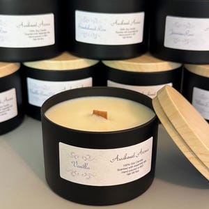 May include: A black candle jar with a wooden lid. The candle is labeled "Vanilla" and "Awakened Aromas 100% Soy Candle Scented with essential oils Hand poured in MO Net Wt 8oz".