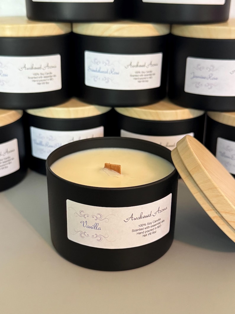 May include: A black candle jar with a wooden lid. The candle is labeled "Vanilla" and "Awakened Aromas 100% Soy Candle Scented with essential oils Hand poured in MO Net Wt 8oz".