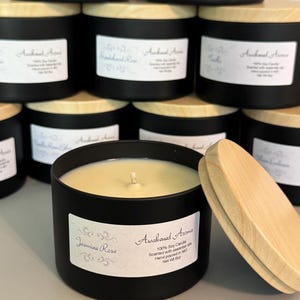 May include: A black candle jar with a wooden lid. The candle is labeled "Awakened Aroma" and "Jasmine Rose". The candle is 100% soy and scented with essential oils. It is hand-poured in Missouri and has a net weight of 8 oz.