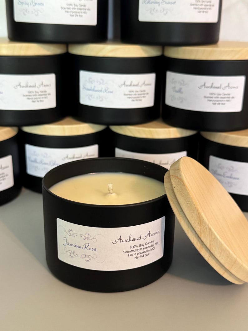May include: A black candle jar with a wooden lid. The candle is labeled "Awakened Aroma" and "Jasmine Rose". The candle is 100% soy and scented with essential oils. It is hand-poured in Missouri and has a net weight of 8 oz.