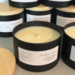 May include: A black candle jar with a wooden lid. The candle is labeled "Jasmine Rose" and "Awakened Aroma" with the text "100% Soy Candle Scented with essential oils Hand poured in MO Net Wt 6 oz".
