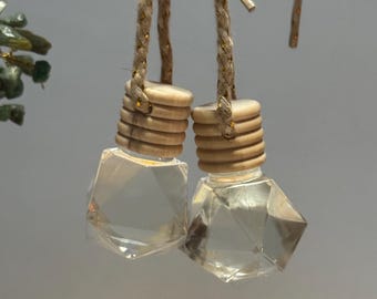 May include: Two clear, faceted glass car air fresheners with wooden caps and braided gold-toned cords. The air fresheners are hanging against a neutral background. The caps are made of stacked wooden rings.