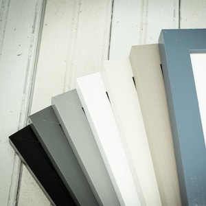 May include: A collection of picture frames in various colors, including black, gray, white, and blue. The frames are arranged in a fan shape, showcasing their different hues and styles. The frames are made of wood and have a clean, modern design.