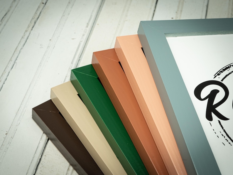 May include: A collection of colorful picture frames in shades of brown, beige, green, orange, and blue. The frames are arranged in a fan shape, showcasing their various colors and textures. The corner of a frame with the letter "R" is visible.