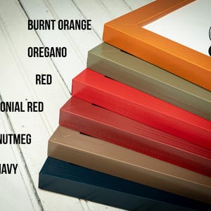May include: A stack of picture frames in various colors, including burnt orange, oregano, red, colonial red, nutmeg, and navy. The frames are angled, showcasing their different hues and textures. The text on the left indicates the color names.