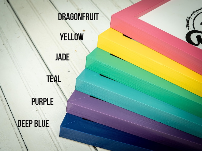 May include: A stack of colorful picture frames in shades of pink, yellow, green, teal, purple, and deep blue. The frames are labeled with color names: Dragonfruit, Yellow, Jade, Teal, Purple, and Deep Blue. The frames are stacked diagonally on a white wooden surface.
