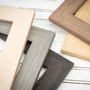 May include: Four different picture frames in various wood tones and finishes. The frames are arranged in a stack, with the top frame being a light brown wood, the second frame being a dark brown wood, the third frame being a gray wood, and the bottom frame being a black wood.