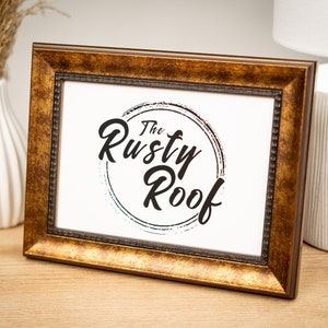 以下が含まれることがあります： 白いマットと「The Rusty Roof」という文字が円形に書かれた黒と白のロゴが入った金色の額縁です。
