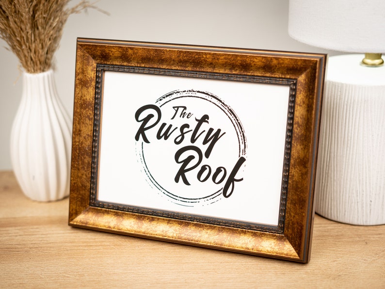 以下が含まれることがあります： 白いマットと「The Rusty Roof」という文字が円形に書かれた黒と白のロゴが入った金色の額縁です。