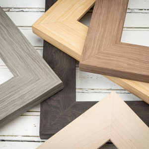 May include: Four different picture frames with various wood finishes. The frames are arranged in a corner shape, with the top frame being a light brown wood, the bottom frame being a light beige wood, and the two side frames being a dark brown wood and a gray wood.